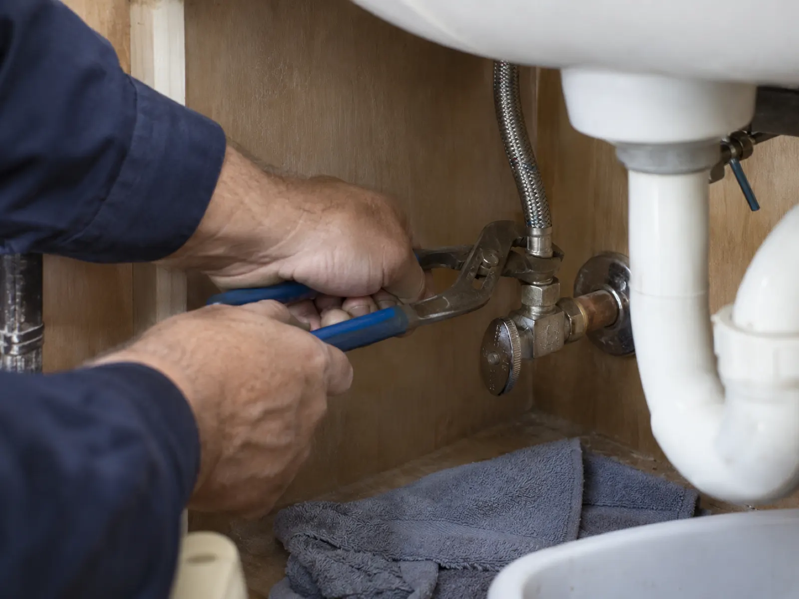 Plumber's hands adjusting a water supply valve underneath a sink during a repair